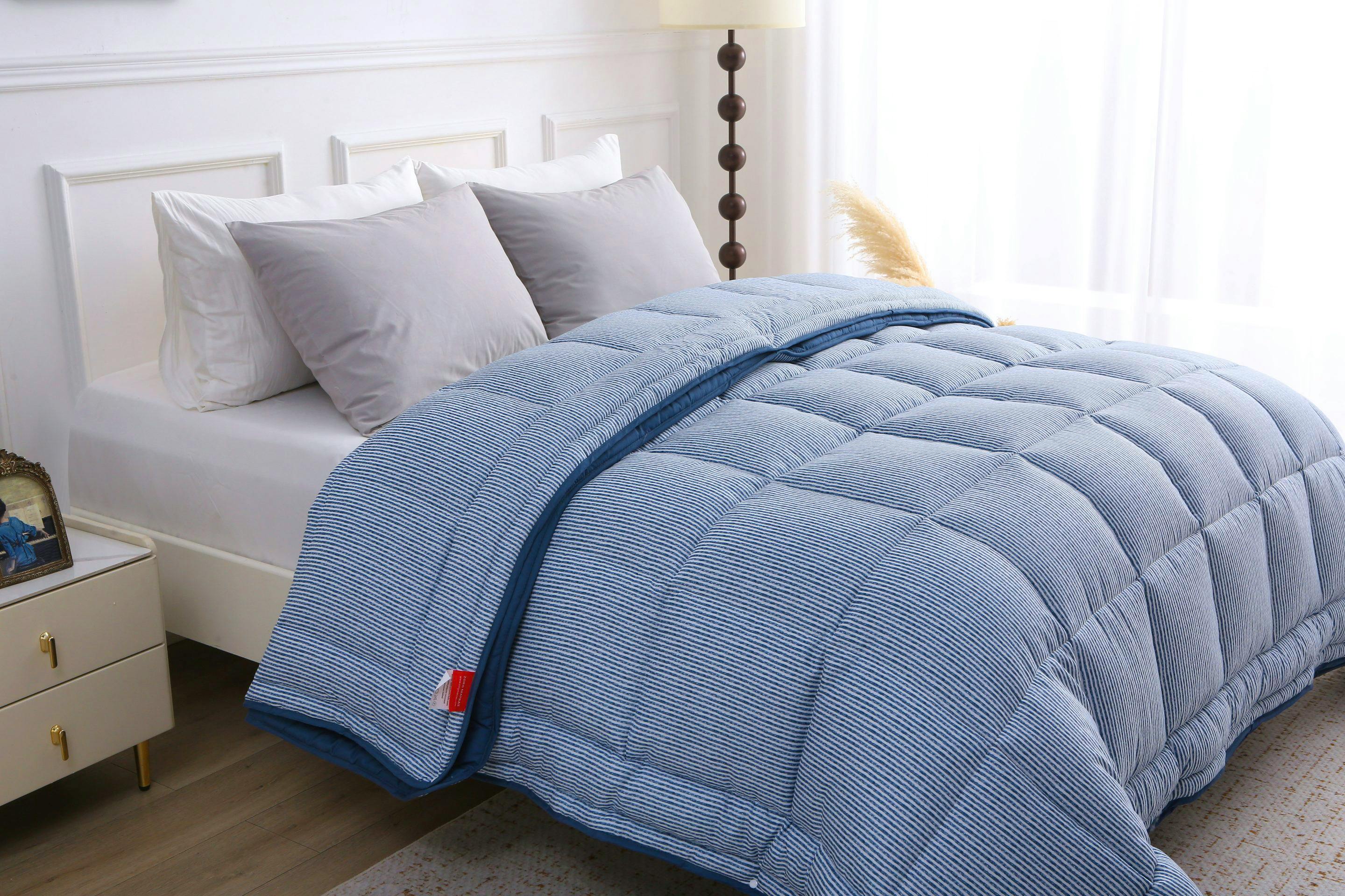 Opgemaakt bed met het blauw-wit gestreepte 4-seizoenen dekbed zonder overtrek, zichtbaar vanuit een zijhoek met lichtinval