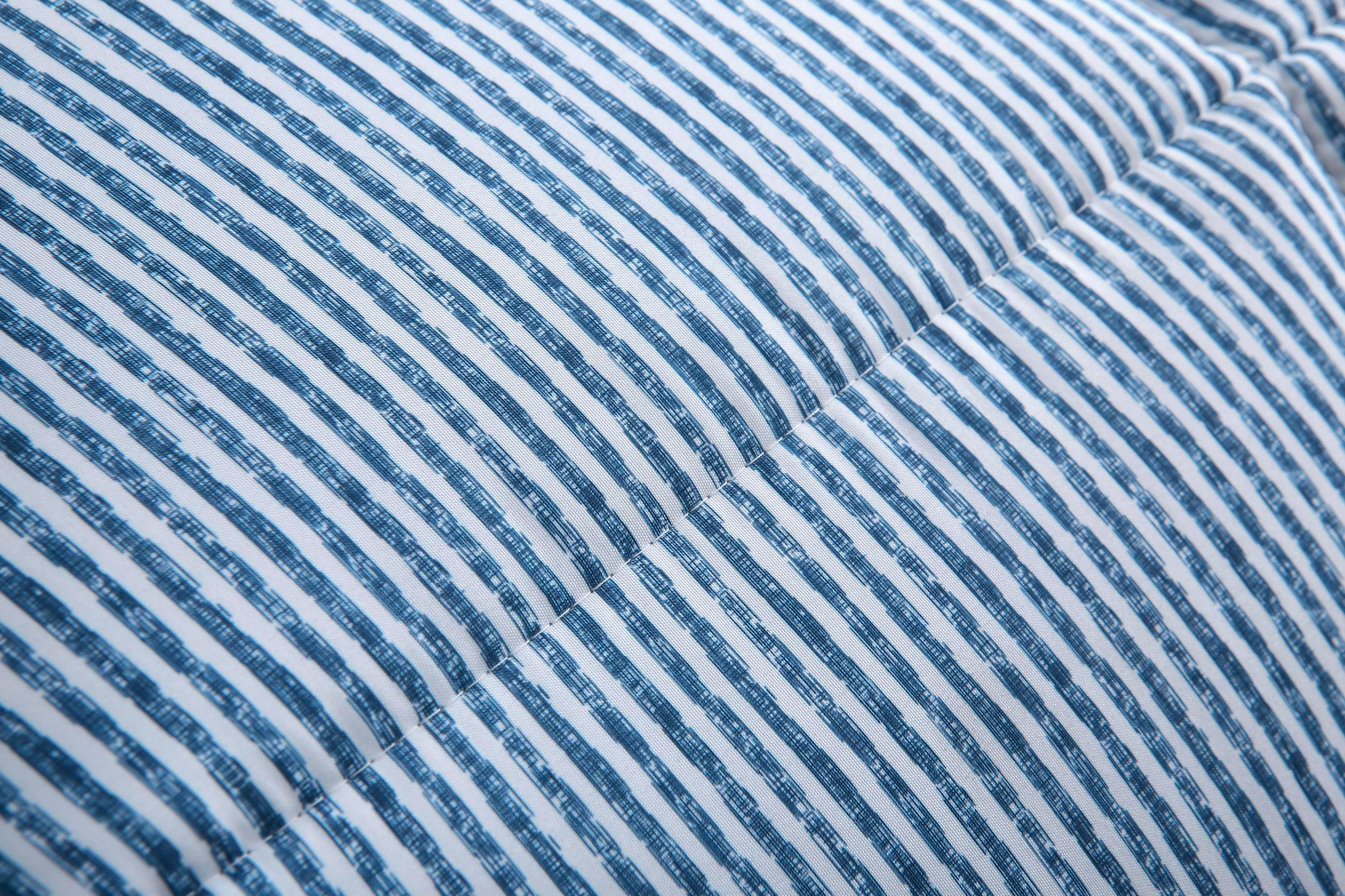 Detailweergave van het blauw gestreepte dekbed met vaste hoes en twee grijze hoofdkussens op de achtergrond.